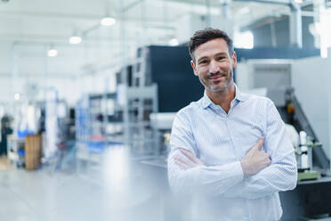 Smiling mature businessman with arms crossed in industry - DIGF13677