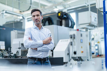 Mature male professional with arms crossed thinking while standing in factory - DIGF13678