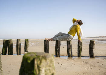 Woman sitting on wooden post at beach against clear sky - UUF22332