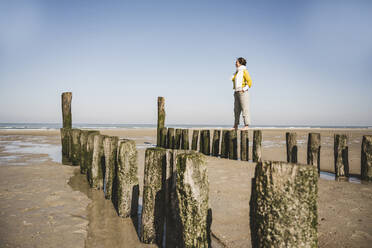 Frau steht auf Holzpfosten am Strand gegen den klaren Himmel an einem sonnigen Tag - UUF22338