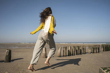 Carefree woman running at beach against clear sky during sunny day - UUF22340