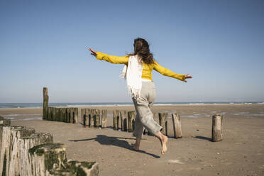 Carefree woman running at beach against clear sky - UUF22341