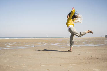 Carefree woman jumping at beach against clear sky during sunny day - UUF22342