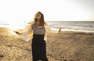 Fröhliche Frau tanzt am Strand gegen den Himmel an einem sonnigen Tag - UUF22349
