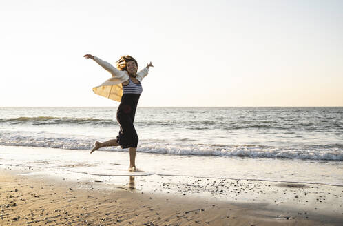 Unbeschwerte junge Frau läuft am Strand gegen den klaren Himmel bei Sonnenuntergang - UUF22360