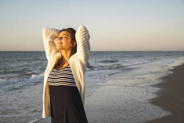 Smiling young woman at beach against clear sky during sunset - UUF22362