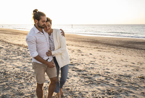 Romantic young couple walking at beach during sunny day stock photo