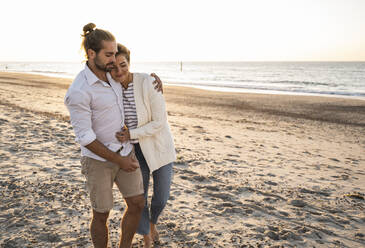 Romantic young couple walking at beach during sunny day - UUF22366