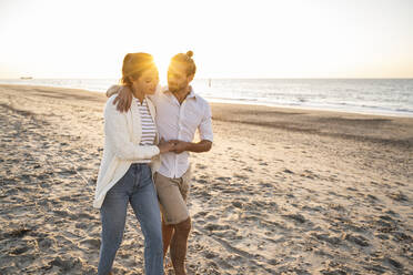 Young couple holding hands while walking at beach during sunny day - UUF22367