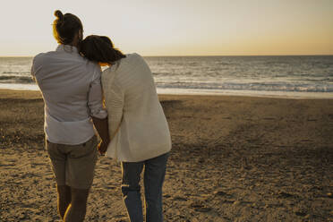 Romantisches Paar, das bei Sonnenuntergang am Strand spazieren geht - UUF22371