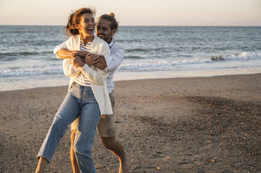 Happy young couple enjoying at beach during sunset - UUF22373