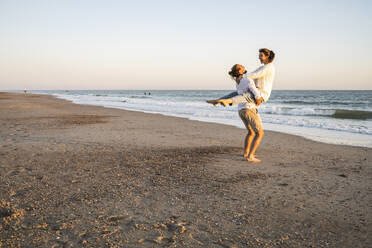 Carefree boyfriend lifting girlfriend at beach during sunset - UUF22376