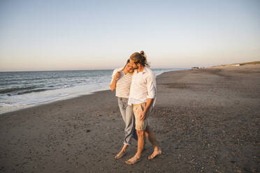 Romantic young couple walking at beach against clear sky during vacation - UUF22383