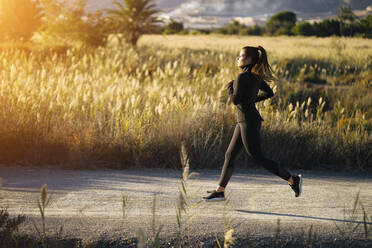 Young woman jogging on footpath against landscape at sunset - MPPF01350