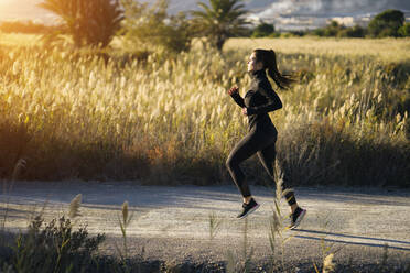 Young woman running on footpath against green landscape at sunset - MPPF01351