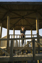 Junge Frau steht am Geländer eines Pavillons bei Sonnenuntergang - MPPF01360