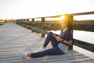 Young woman using smart phone while sitting on footbridge against clear sky - MPPF01368