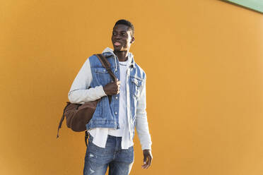Junger Mann, der einen Rucksack trägt, während er an einer gelben Wand an einem sonnigen Tag steht - MPPF01379