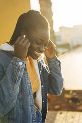 Lächelndes jugendliches Mädchen mit In-Ear-Kopfhörern auf der Straße - MPPF01382