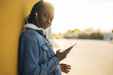 Teenager-Mädchen mit Mobiltelefon hört Musik und lehnt sich an die Wand - MPPF01385