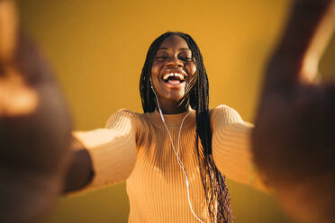 Lachendes Teenager-Mädchen mit ausgestreckten Armen, das Musik gegen eine gelbe Wand hört - MPPF01394