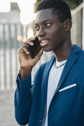 Junger Geschäftsmann im Blazer, der im Freien mit einem Mobiltelefon telefoniert - MPPF01398
