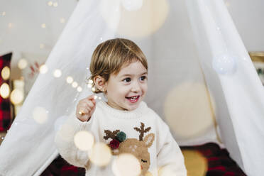Niedliches kleines Mädchen, das wegschaut, während es zu Hause an einem Zelt steht, während Weihnachten - EBBF01950