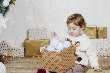 Baby-Mädchen hält Weihnachtsbeleuchtung in Geschenk-Box, während zu Hause sitzen - EBBF01955