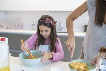 Daughter preparing muffin standing by mother in kitchen - SNF00890