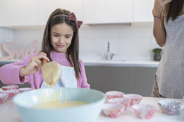 Daughter looking at batter standing by mother in kitchen - SNF00892