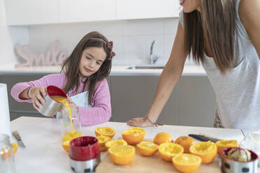 Daughter pouring orange juice in jar standing by mother in kitchen - SNF00902