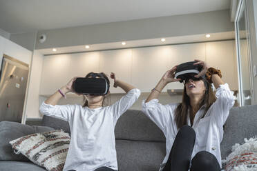 Mother using virtual reality glasses with her daughter while sitting on sofa in living room - SNF00908