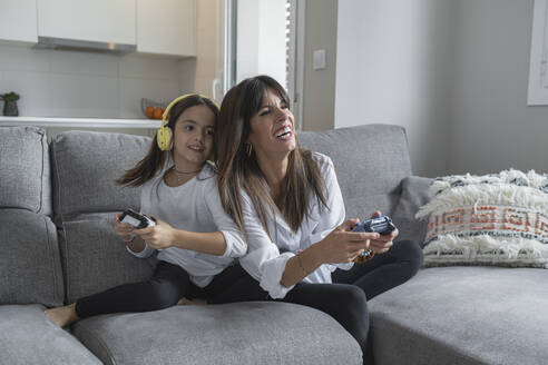 Smiling mother and daughter playing video games together at home - SNF00917