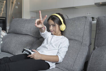 Kleines Mädchen macht Friedenszeichen, während es im Wohnzimmer ein Videospiel spielt - SNF00923
