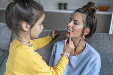 Daughter applying red lipstick to mother in living room at home - SNF00932