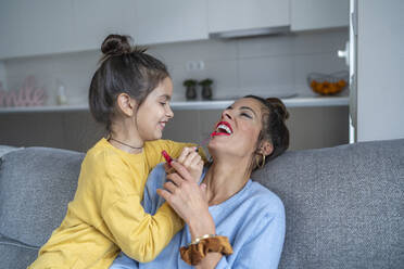 Smiling daughter applying lipstick to mother in living room at home - SNF00933