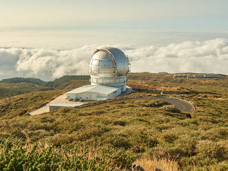 Das größte optische Spiegelteleskop Gran Telescopio Canarias steht auf einem grasbewachsenen Hügel vor einem bewölkten Himmel in der Sternwarte auf der Insel La Palma in Spanien - ADSF19683