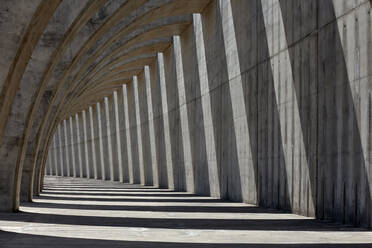 Columns of empty concrete walkway illuminated by sunlight casting lines of shadow on stone wall - ADSF19688