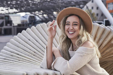 Cheerful young woman wearing hat standing by patterned retaining wall - SUF00655