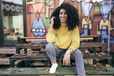 Beautiful woman with curly hair sitting on steps in city during autumn - SUF00665