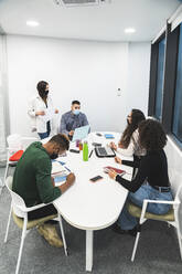 Creative male and female colleagues discussing while sitting in board room at office - JAQF00061