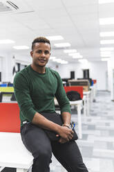 Smiling young businessman with file document siting on desk at work place - JAQF00066