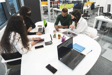 Businessman with female colleagues discussing over diary in board room at work place - JAQF00072