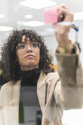 Young businesswoman writing new ideas on adhesive note at office - JAQF00092