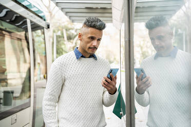 Spiegelung eines männlichen Unternehmers, der ein Smartphone am Bahnhof hält - AFVF07927