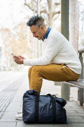 Male entrepreneur using smart phone while sitting at bus stop - AFVF07930
