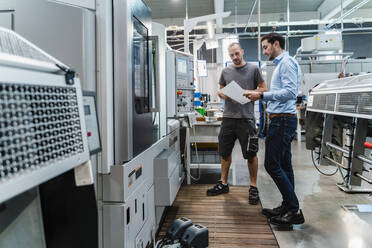 Engineer discussing over document with coworker while standing by equipment at industry - DIGF13728