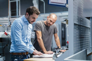Männliche Ingenieure analysieren einen Plan, während sie an einem Tisch in der Industrie stehen - DIGF13732