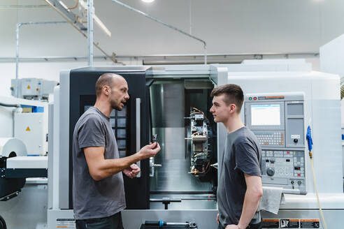 Maintenance engineer giving instruction to coworker while standing against machinery at industry - DIGF13735