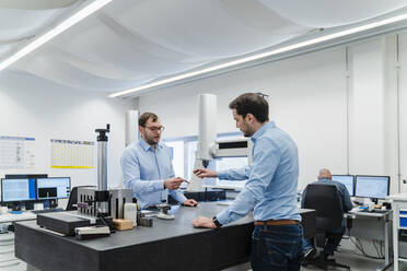 Engineers discussing over equipment while standing with coworker in background at office - DIGF13758